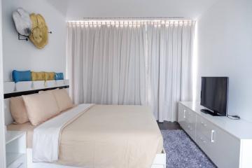 Modern bedroom with a neatly made bed, a flat-screen TV, and streamlined white furnishings