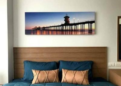 Cozy bedroom with a wall-mounted seaside photograph above a bed with blue bedding and decorative pillows