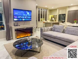 Spacious living room with modern furniture, electric fireplace, and open kitchen in the background