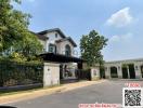 Exterior view of a luxurious two-story house with a landscaped garden and gated entrance