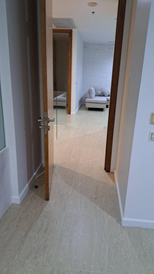 View of a corridor with tiled floors leading towards a bedroom with a visible bed and pillows