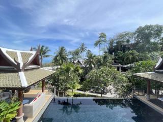 Bright and serene outdoor pool area with tropical trees and traditional-style buildings