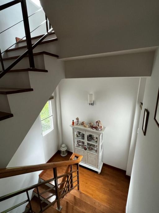 Interior view of a staircase with wooden steps and railing leading to an upper level, featuring a small wooden cabinet and decorative items