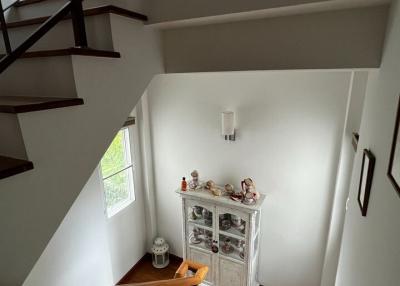 Interior view of a staircase with wooden steps and railing leading to an upper level, featuring a small wooden cabinet and decorative items