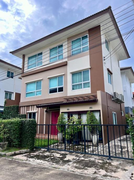 Three-story residential home with tan and brown exterior, front gate, and small garden area