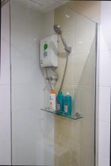 A modern electric shower with toiletries on a glass shelf in a tiled bathroom