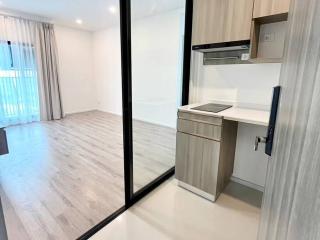 Modern apartment interior with an open kitchen and empty living space featuring large windows and wooden flooring