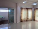 Spacious living room with tiled flooring, large windows, and elegant curtains