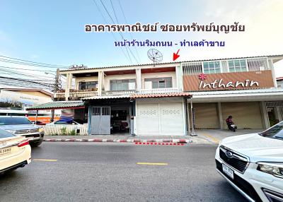 Two-story commercial-residential building with signage, parked cars, and a clear sky