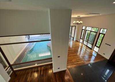 Spacious interior with view of the pool through large windows, featuring hardwood flooring and elegant chandelier