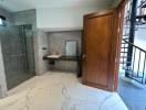 Modern bathroom interior with marble flooring, glass shower area, and wooden door