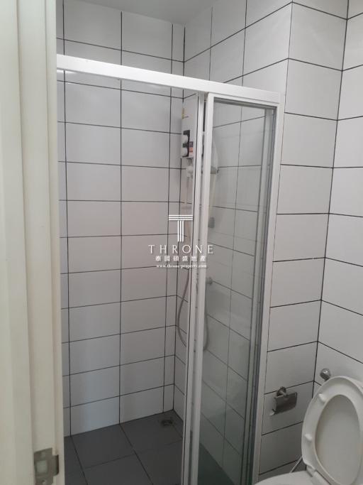 Small white tiled bathroom with glass shower door and toilet