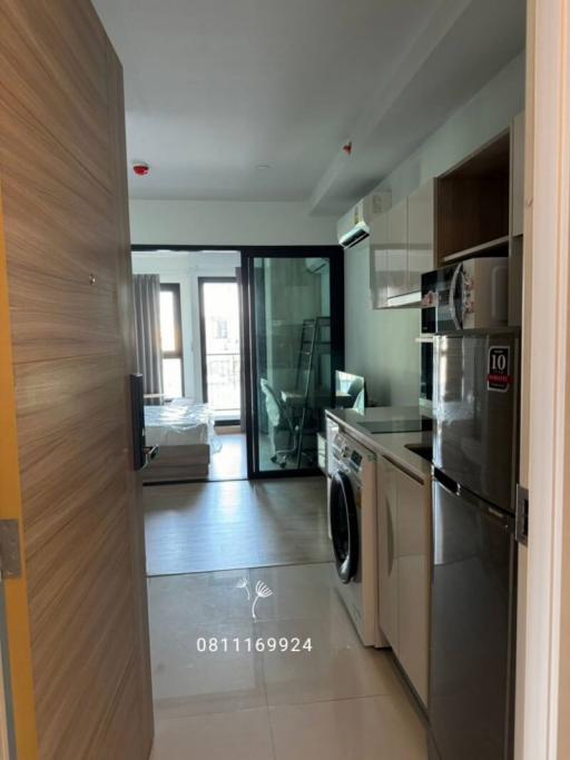 Compact apartment interior showing hallway with kitchenette and washing machine leading to living area with large window