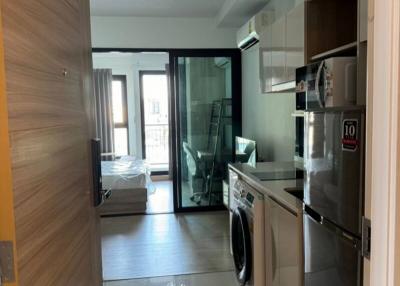 Compact apartment interior showing hallway with kitchenette and washing machine leading to living area with large window