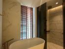 Elegant bathroom with freestanding tub, marble tiling, and natural light