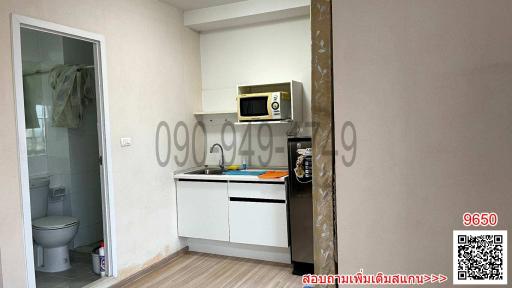 Compact kitchen space with white cabinets and a microwave next to an open bathroom door