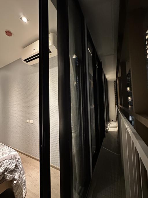 Narrow corridor inside a home with partial view of a bedroom, showing wood flooring, lighting, and frosted glass doors