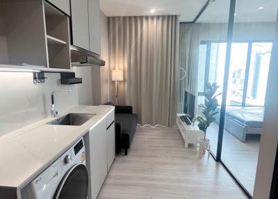 Modern laundry area with washing machine aside a compact living space with large windows and abundant natural light