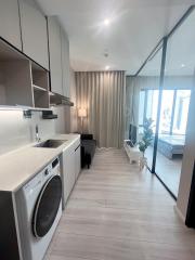 Modern laundry area with washing machine aside a compact living space with large windows and abundant natural light