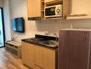Compact modern kitchen with wooden cabinets, appliances, and TV