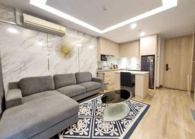 Compact modern living room with an open kitchen design, featuring a grey sofa, blue and white patterned rug, and wooden furniture