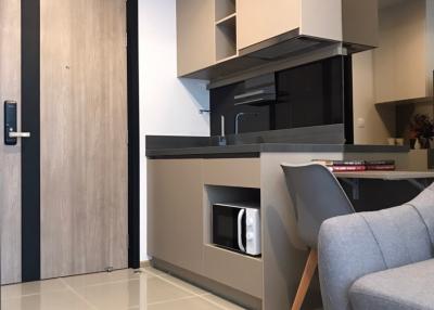 Modern compact kitchen space with sleek appliances and light wood cabinetry adjacent to a cozy living area