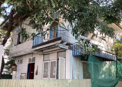 Two-story house with weathered blue and white paint surrounded by greenery