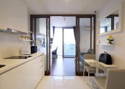 Modern compact kitchen with white cabinets and appliances leading to a cozy living area with balcony access