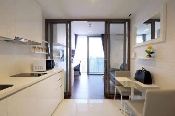 Modern compact kitchen with white cabinets and appliances leading to a cozy living area with balcony access