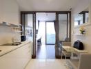 Modern compact kitchen with white cabinets and appliances leading to a cozy living area with balcony access