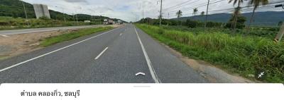 Paved road with greenery and mountains under a cloudy sky