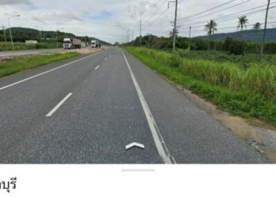 Paved road with greenery and mountains under a cloudy sky