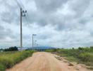Unpaved country road with power lines and cloudy sky