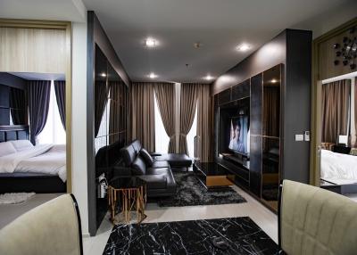 Modern bedroom with connected living area featuring a large bed, black sofa, and flat-screen TV