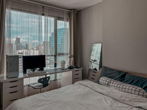 Modern bedroom with city view, featuring a work desk and large windows