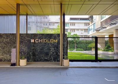 Elegant building entrance with large marble wall and gate leading to a green outdoor area