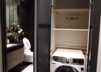 Modern bathroom with integrated laundry space, featuring a washing machine, marble flooring, and sophisticated dark tones