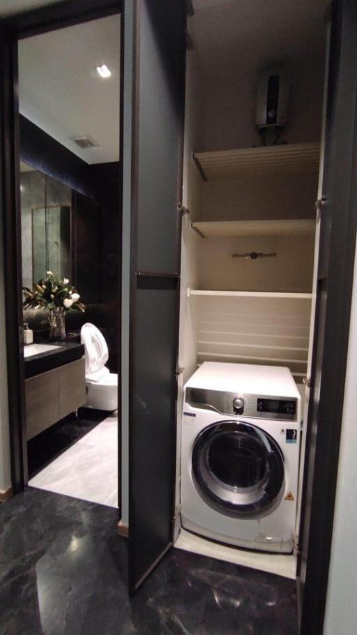 Modern bathroom with integrated laundry space, featuring a washing machine, marble flooring, and sophisticated dark tones