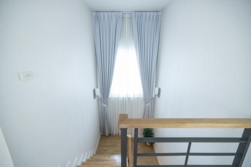 Bright stairway with wooden handrail and large window with curtains