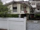 Two-story residential building with white exterior walls and gated entrance