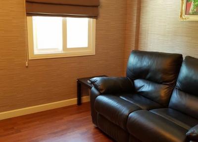 Cozy living room with a comfortable black leather couch, wooden floors, and window blinds