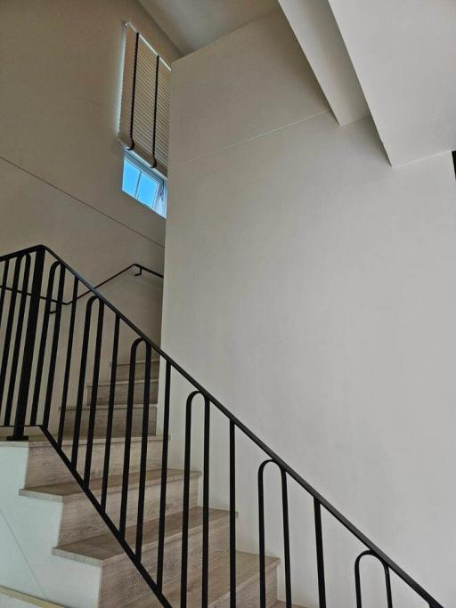 Modern staircase with wooden steps and black metal railing leading to an upper floor with natural light from a high window