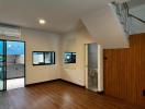 Spacious living area with wooden flooring, kitchen view, staircase, and balcony access