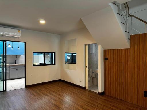 Spacious living area with wooden flooring, kitchen view, staircase, and balcony access