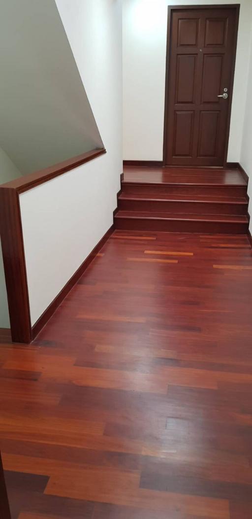 Wooden staircase with polished hardwood floors leading to a closed door