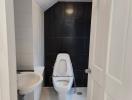 Compact bathroom with white and black tiling featuring a toilet and sink