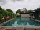 Modern residential outdoor pool surrounded by lush greenery and decorative flamingos