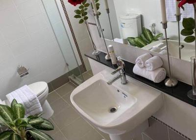Modern bathroom with white fixtures, decorated with plants and red flowers
