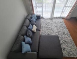 Cozy living room with a gray sectional sofa, patterned cushions, and a large window with sheer curtains