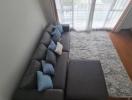 Cozy living room with a gray sectional sofa, patterned cushions, and a large window with sheer curtains